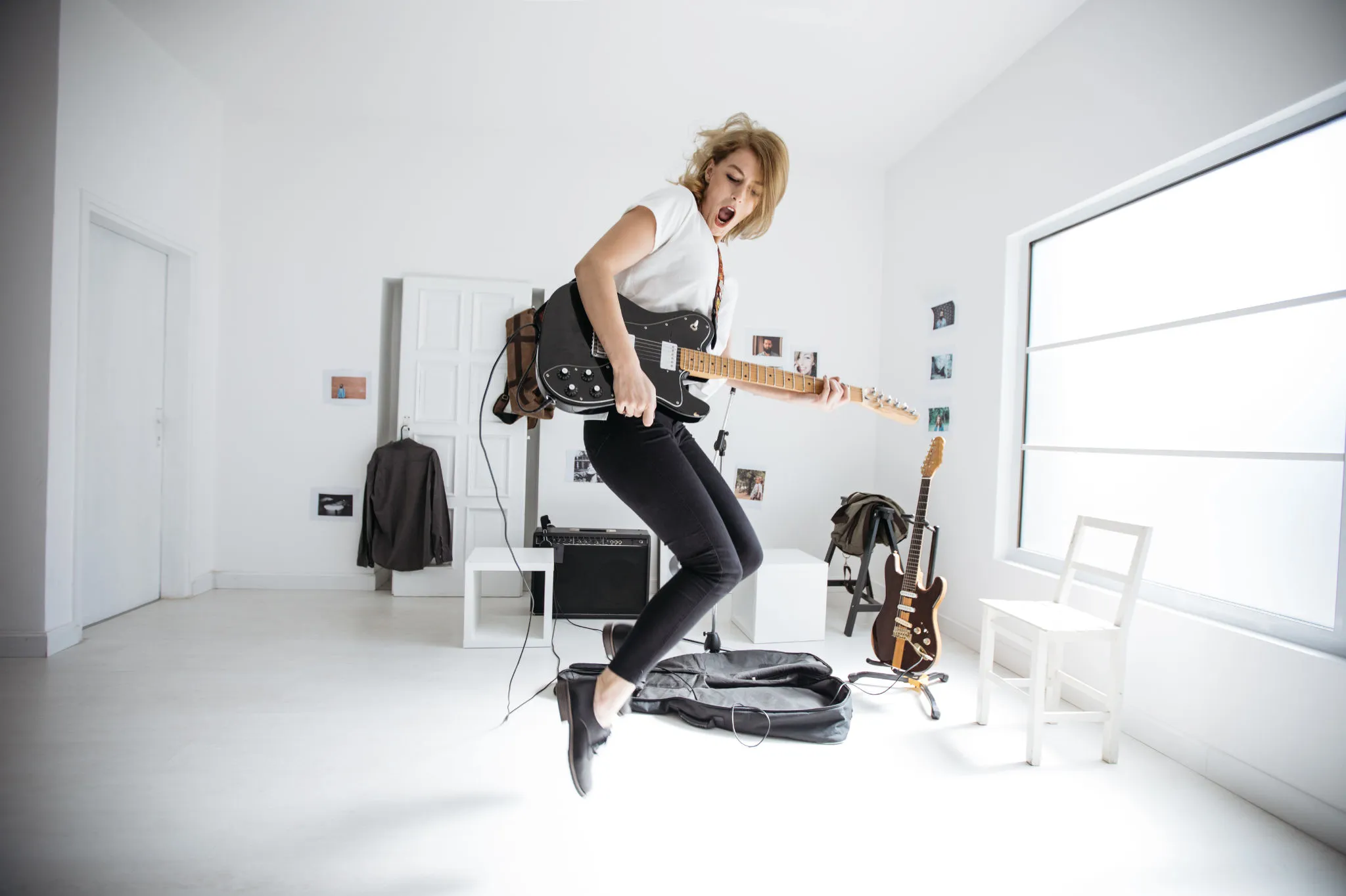 Frau springt mit einer E-Gitarre in einem hellen Raum